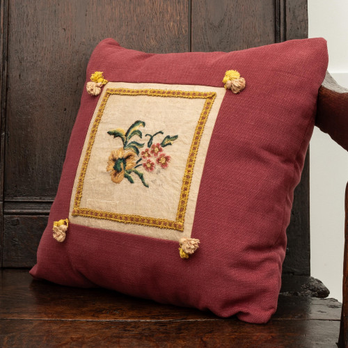 A cushion showcasing a fragment of 18th century crewel embroidery, circa 1710-20